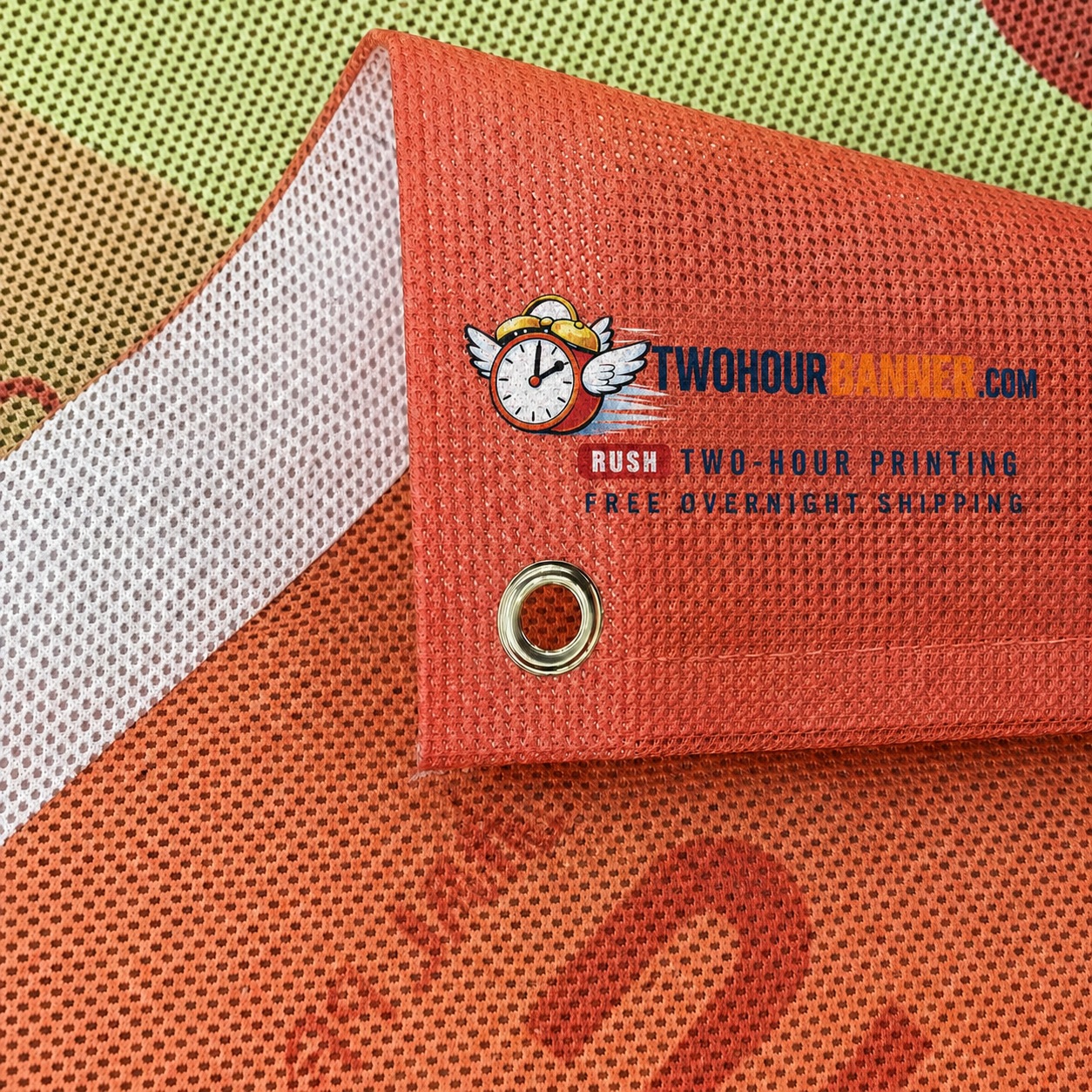 Custom mesh banner material close-up showing TWOHOURBANNER.com logo and brass grommets